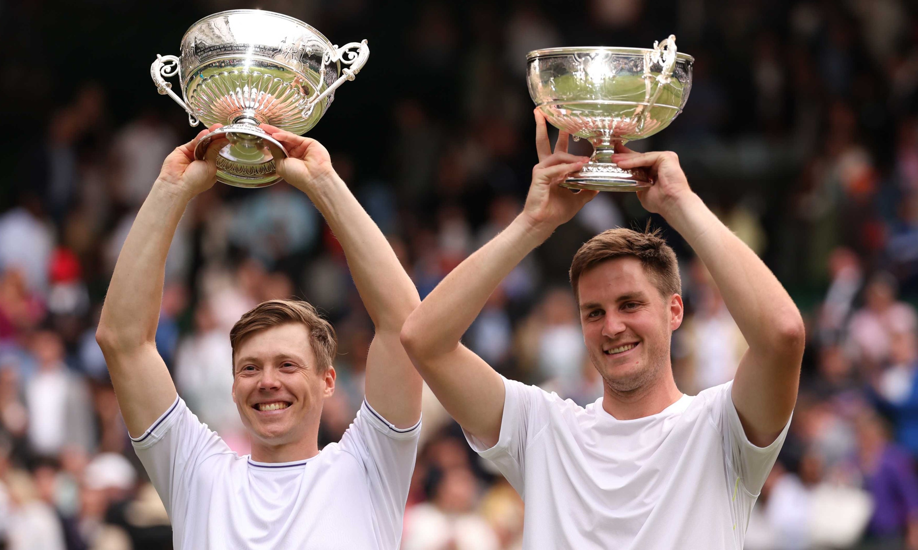 Harri Heliovaara and Henry Patten holding their Wimbledon trophies above their heads while smiling